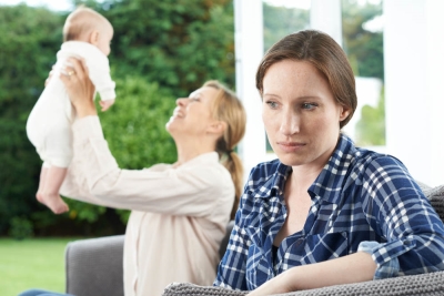 A sad woman in the foreground while another mother is playing with a baby in the background