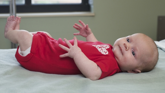 A baby in a red onesie laying on a hospital bed.