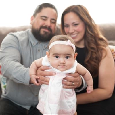 Elena Elias and her husband, sitting on a couch and holding their baby daughter in front of them