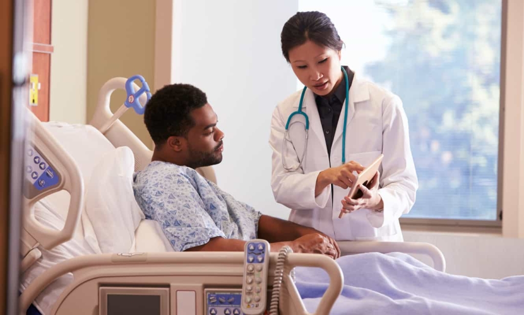 A physician showing a patient laying in bed information from a tablet