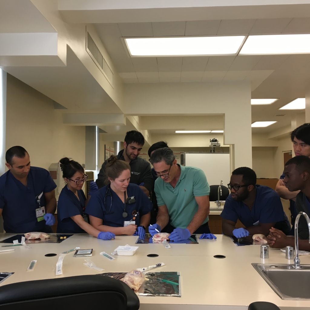 A doctor practicing suturing in front of other residents
