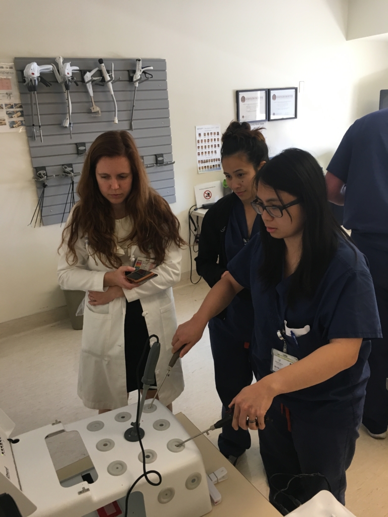 A resident practicing with a machine while two other residents look on.