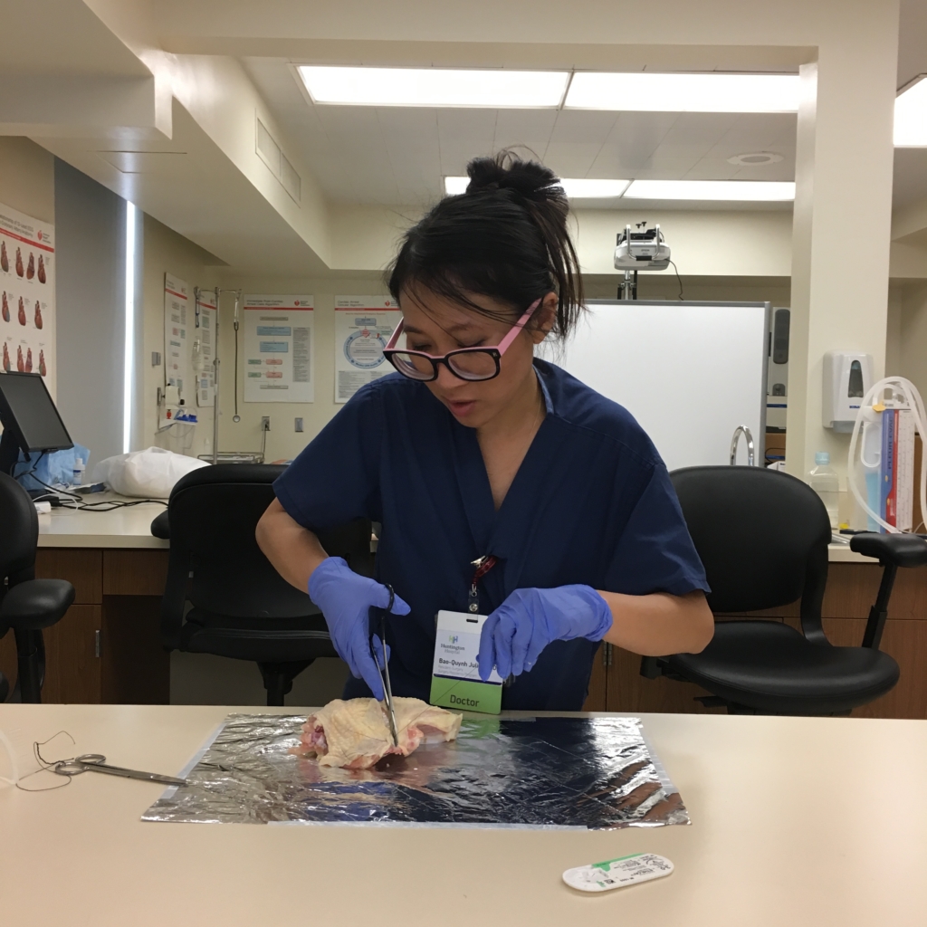 A doctor performing a practice suture on a piece of chicken
