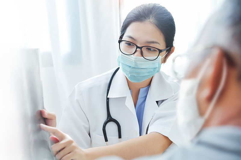 Female asian physician pointing to xrays with male patient watching