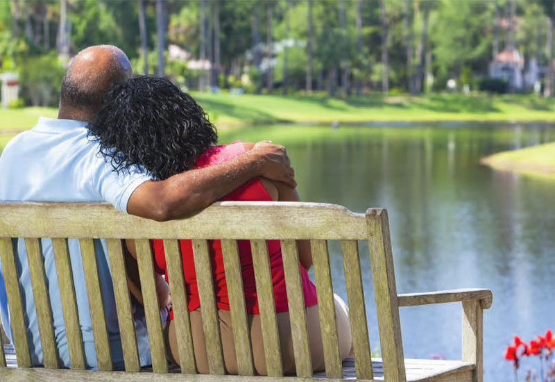 Senior couple sitting on park bench with arms around each other