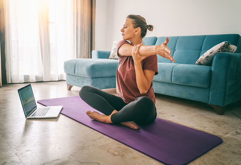 Woman doing yoga in living room with laptop