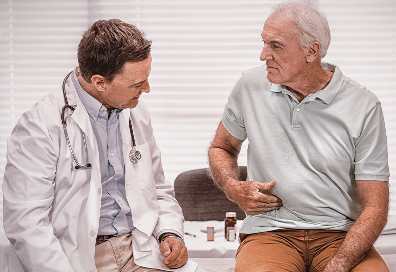 Doctor speaking to senior man, who is pointing to his stomach pain