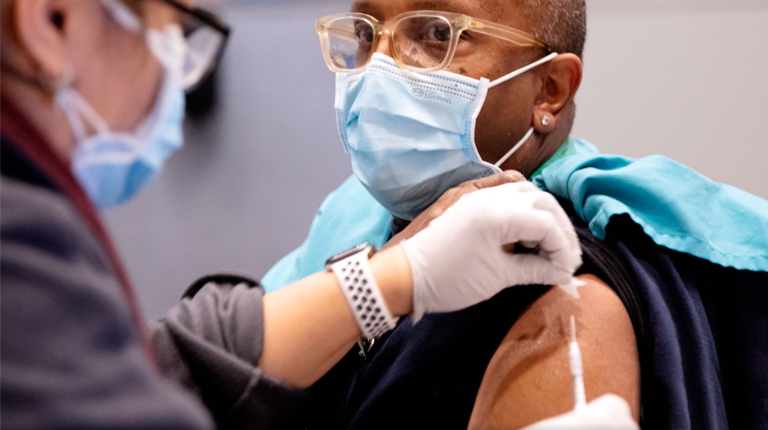 Masked woman receiving a flu shot from a nurse