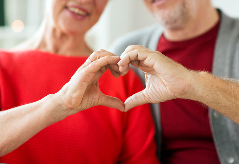 Senior couple, wearing red, holding their hands together to form a heart shape