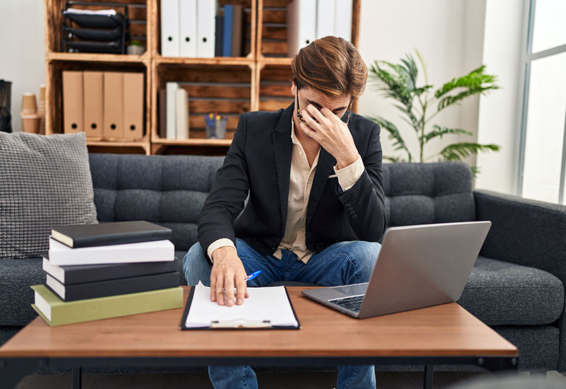 Therapist sitting on couch with hand on his face, looking stressed out