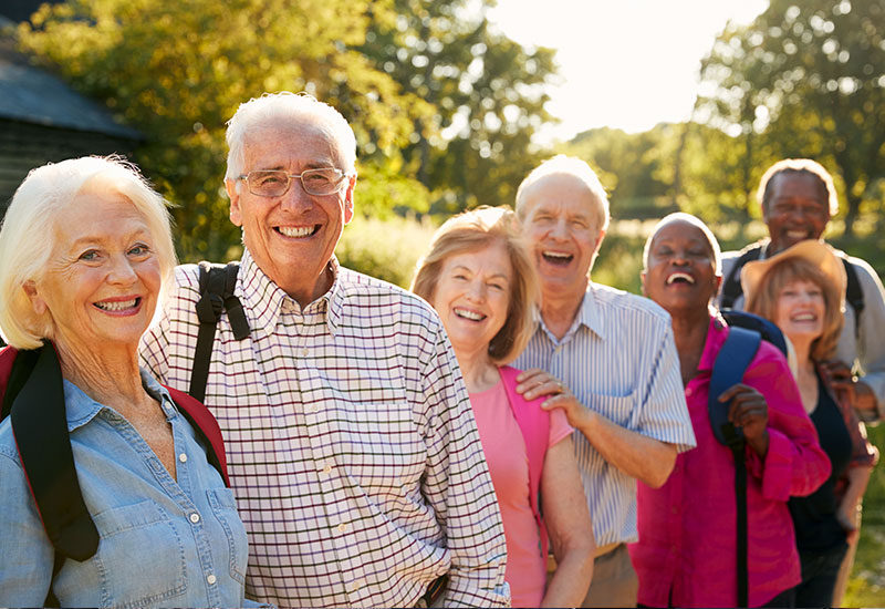 A group of seven seniors, outside, smiling, with hiking backpacks on their backs