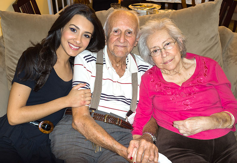 Young brunette girl sitting on a couch, smiliing and leaning against her elderly grandparents