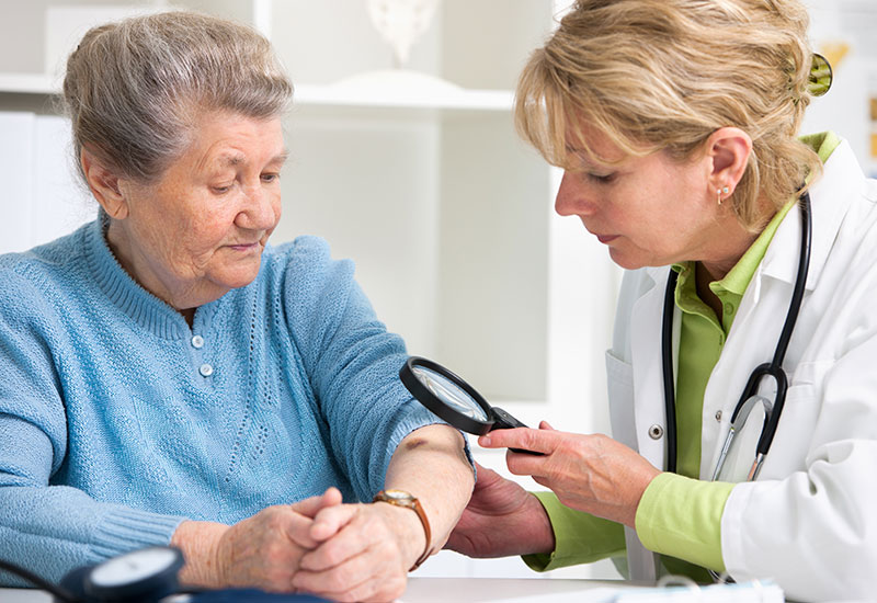 Doctor using a magnifying glass to inspect patient's skin