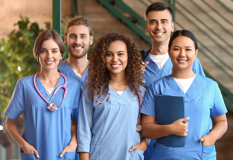 Five nurses standing in scrubs, smiling