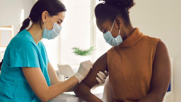 Masked nurse administering vaccine injection to masked patient