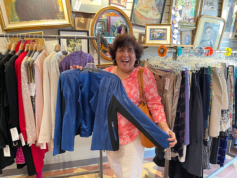 Huntington Collection: A woman is laughing and happy as she holds up an article of clothing next to clothing racks