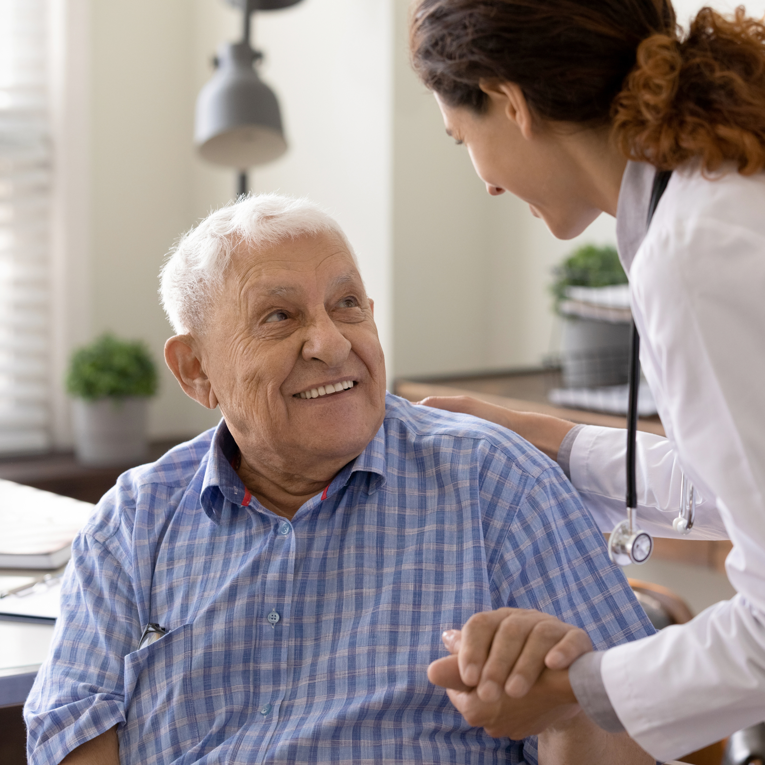 Close up caring nurse holding smiling mature patient hand at meeting in hospital, doctor caregiver wearing uniform comforting and supporting senior man, good news about treatment, empathy and care