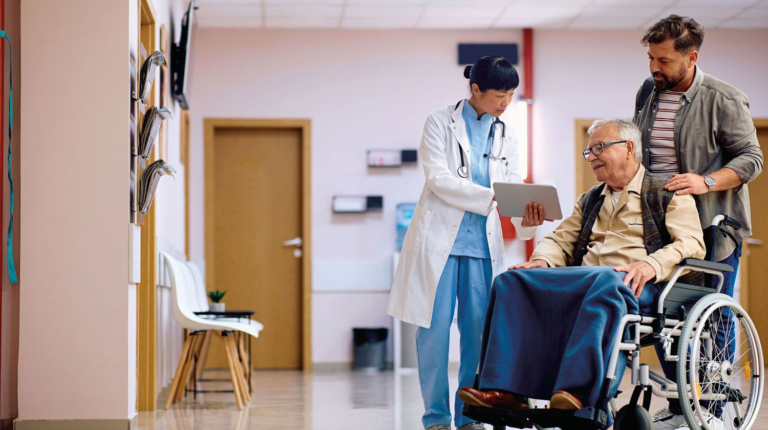 Son with father in wheelchair, talking to doctor sho is showing them something on a tablet