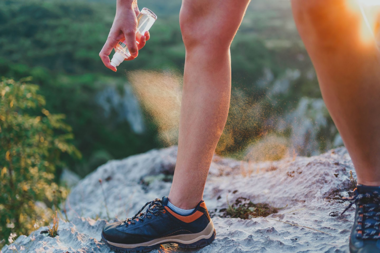 Hiker spraying insect repellent on leg outdoors