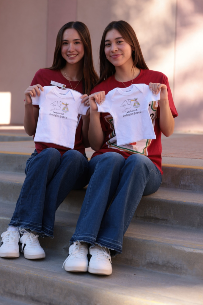 Twin sisters holding Huntington Hospital baby onesies on steps