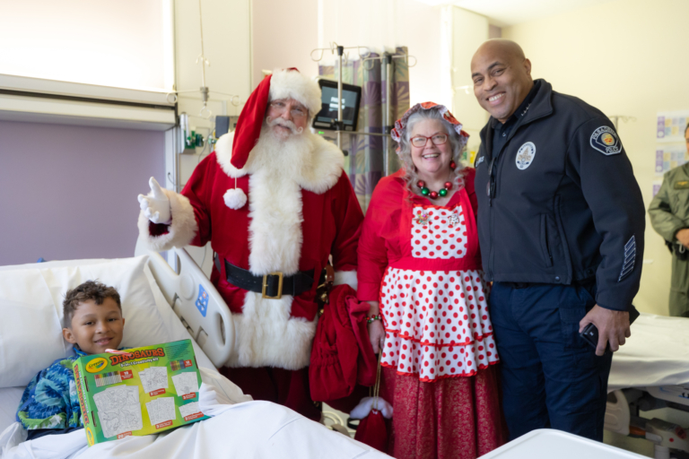 Police officer, Mrs. Claus, and Santa visiting child in hospital