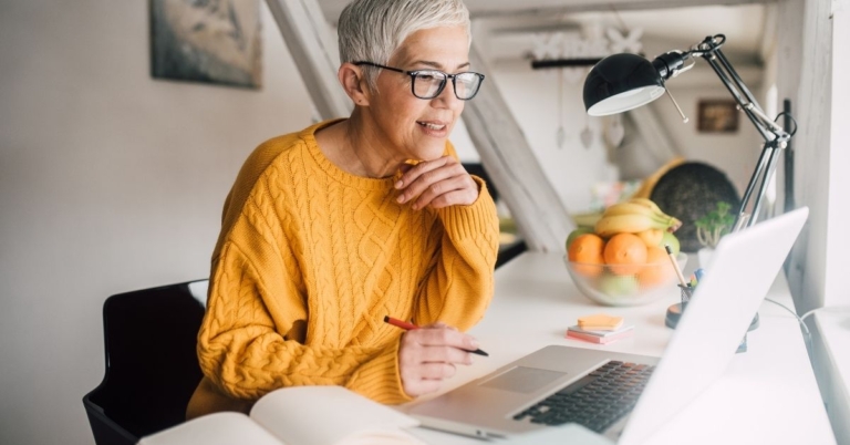 Woman in a yellow sweater working on a laptop.