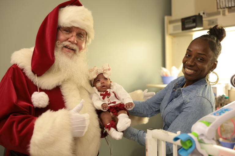 Santa Claus posing with a woman and an infant in the NICU.